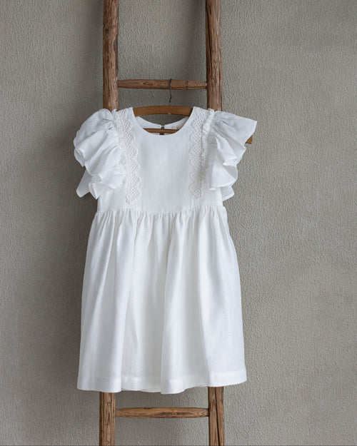 White linen dress with ruffled sleeves and crochet lace on a wooden ladder against a gray wall