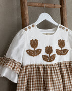Baby linen dress with crocheted flowers on a hanger against a beige wall.