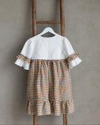 White linen blouse with brown checkered linen skirt hanging on a wooden ladder against a gray wall.