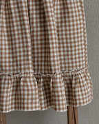 Brown and white checkered linen skirt with ruffle hem on a wooden stool against a gray wall.