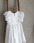 White linen dress with ruffled sleevesand crochet lace on a wooden ladder against a beige wall