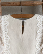 Beige linen dress with crochet lace details on a wooden hanger against a neutral background