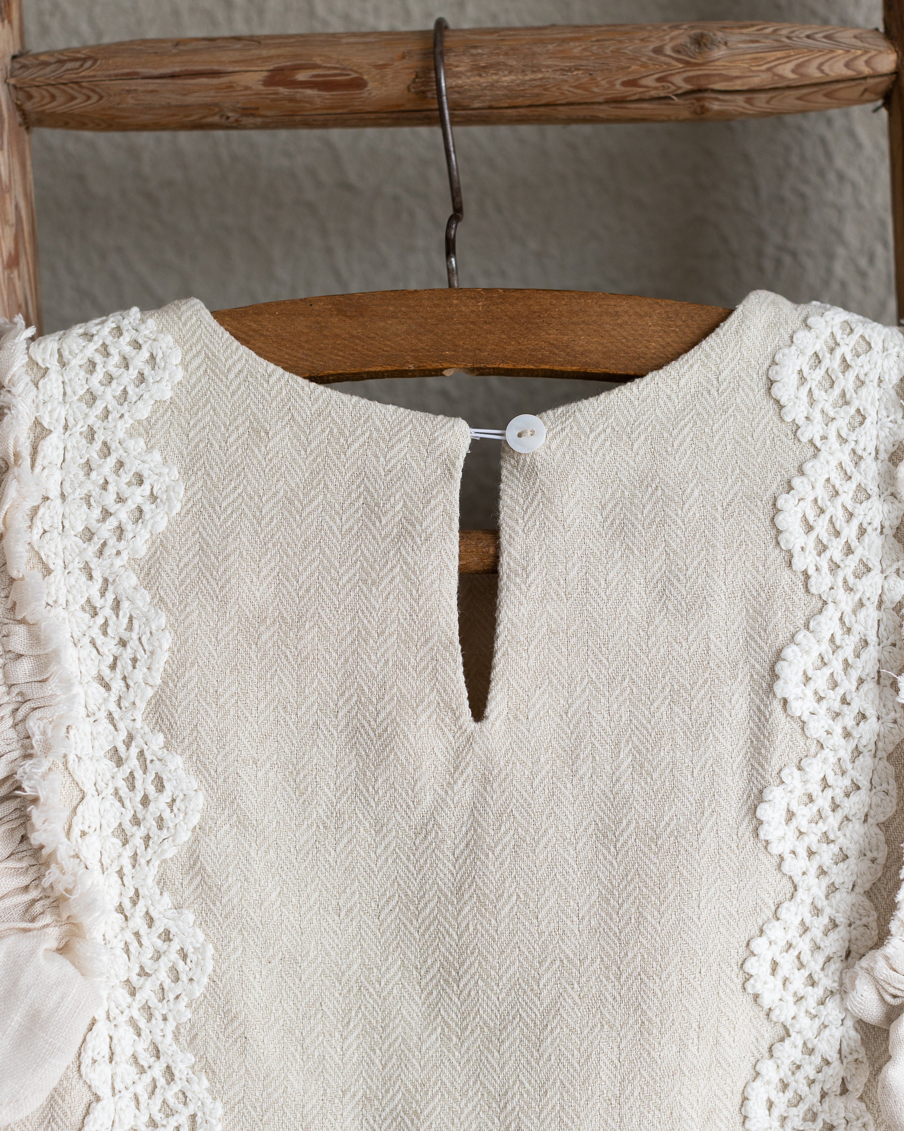 Beige linen dress with crochet lace details on a wooden hanger against a neutral background