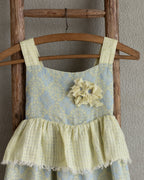 Girls linen flolar dress with flower brooch hanging on a wooden ladder against a plain wall.
