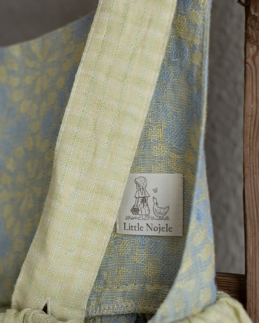 Linen flower dress for little girl with 'Little Noele' label on a wooden ladder