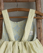 Vintage linen dress for girls with floral pattern and yellow straps on a wooden hanger against a plain wall.