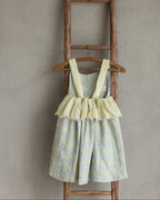 Girl's floral linen dress with ruffled skirt on a wooden hanger against a beige wall.