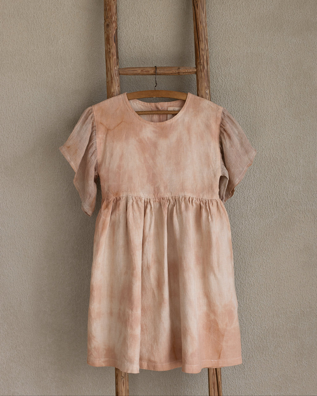 Peach pink linen tie-dye dress on a wooden hanger against a beige wall