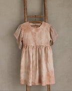 Peach pink linen tie-dye dress on a wooden hanger against a beige wall