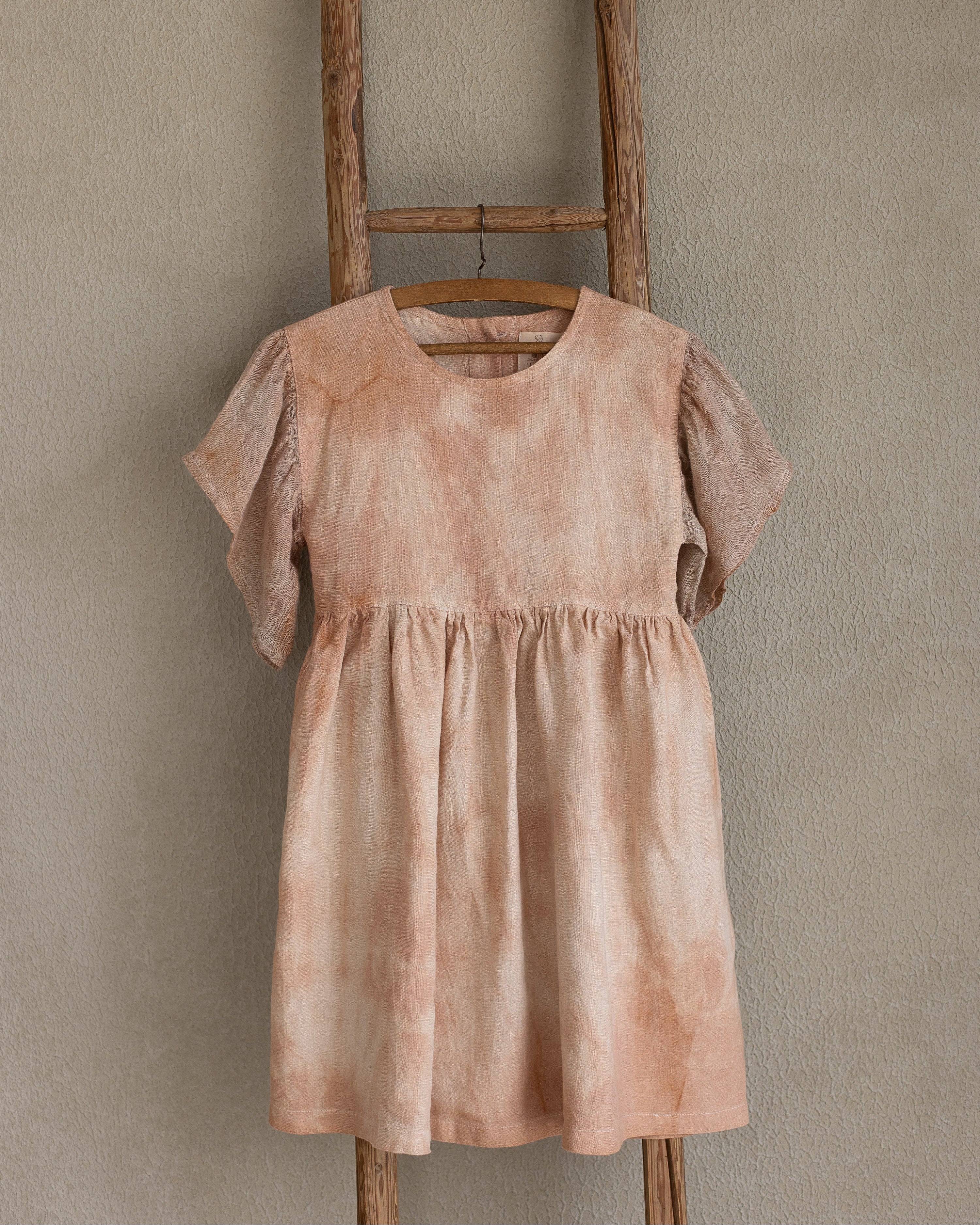 Peach pink linen tie-dye dress on a wooden hanger against a beige wall