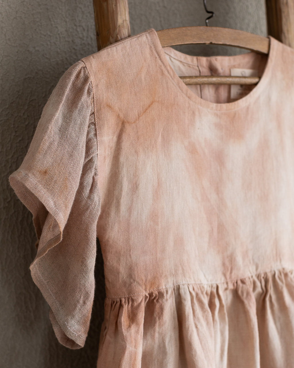Peach pink linen tie-dye dress on a wooden hanger against a beige wall