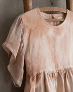 Peach pink linen tie-dye dress on a wooden hanger against a beige wall