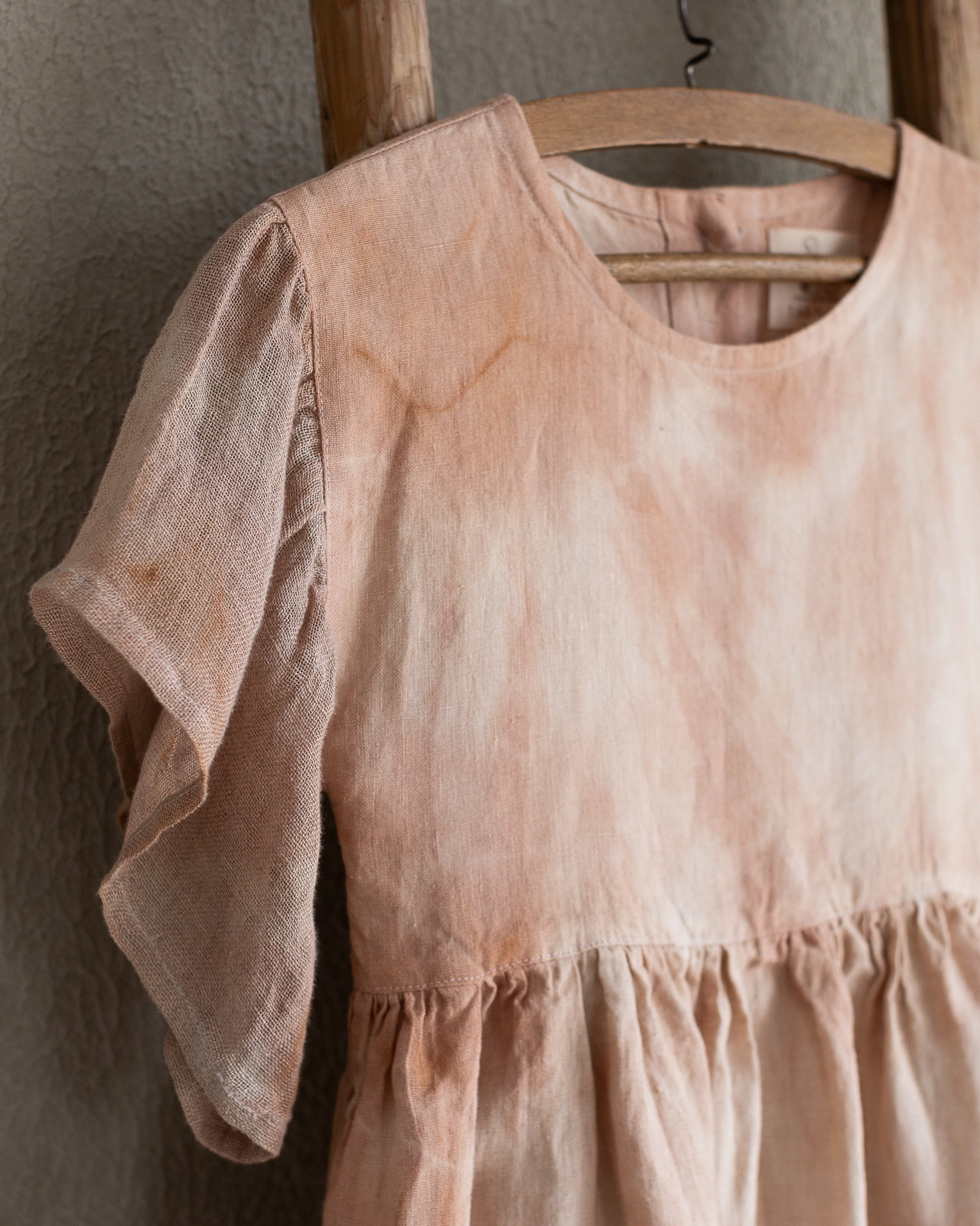 Peach pink linen tie-dye dress on a wooden hanger against a beige wall
