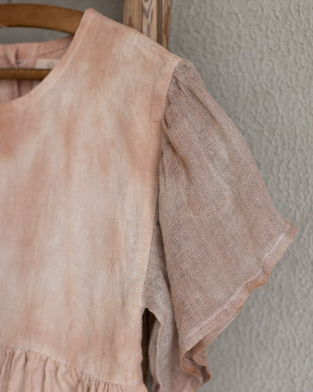 Peach pink linen tie-dye dress on a wooden hanger against a beige wall