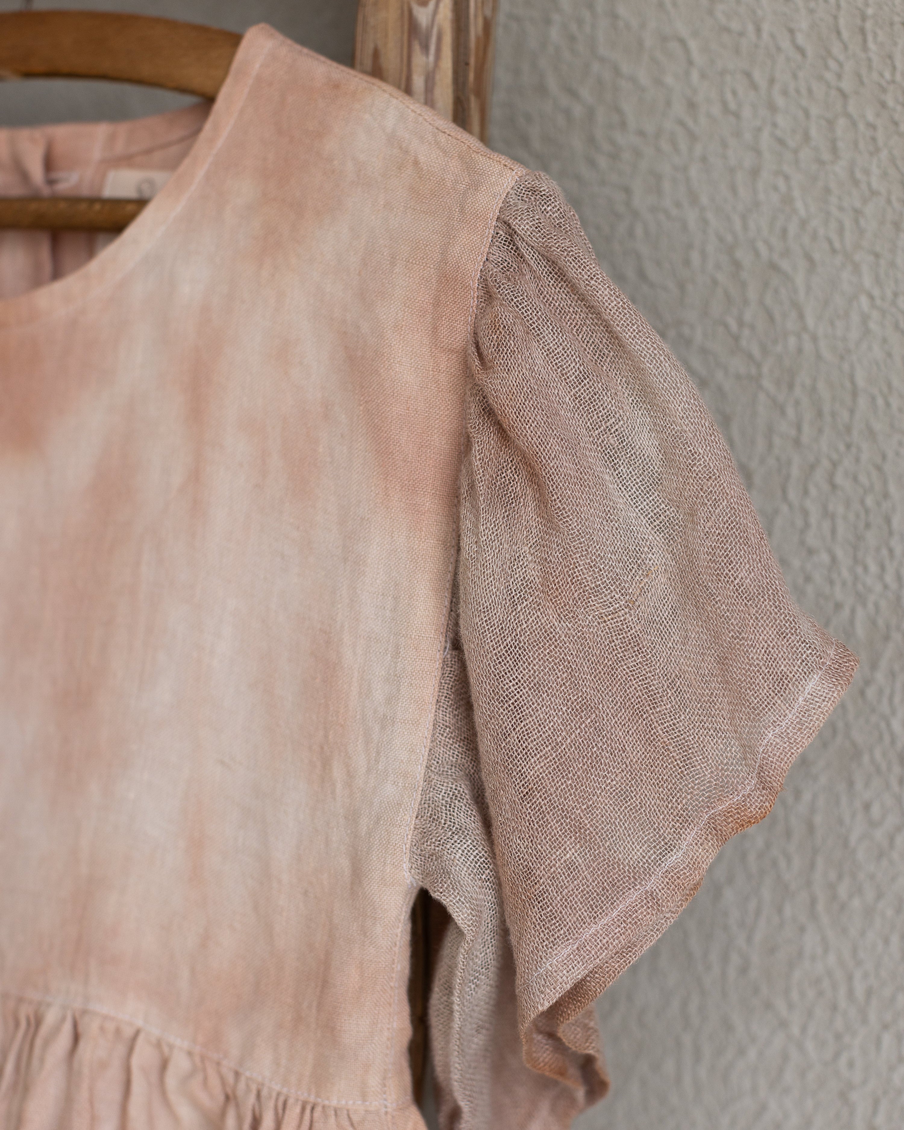 Peach pink linen tie-dye dress on a wooden hanger against a beige wall