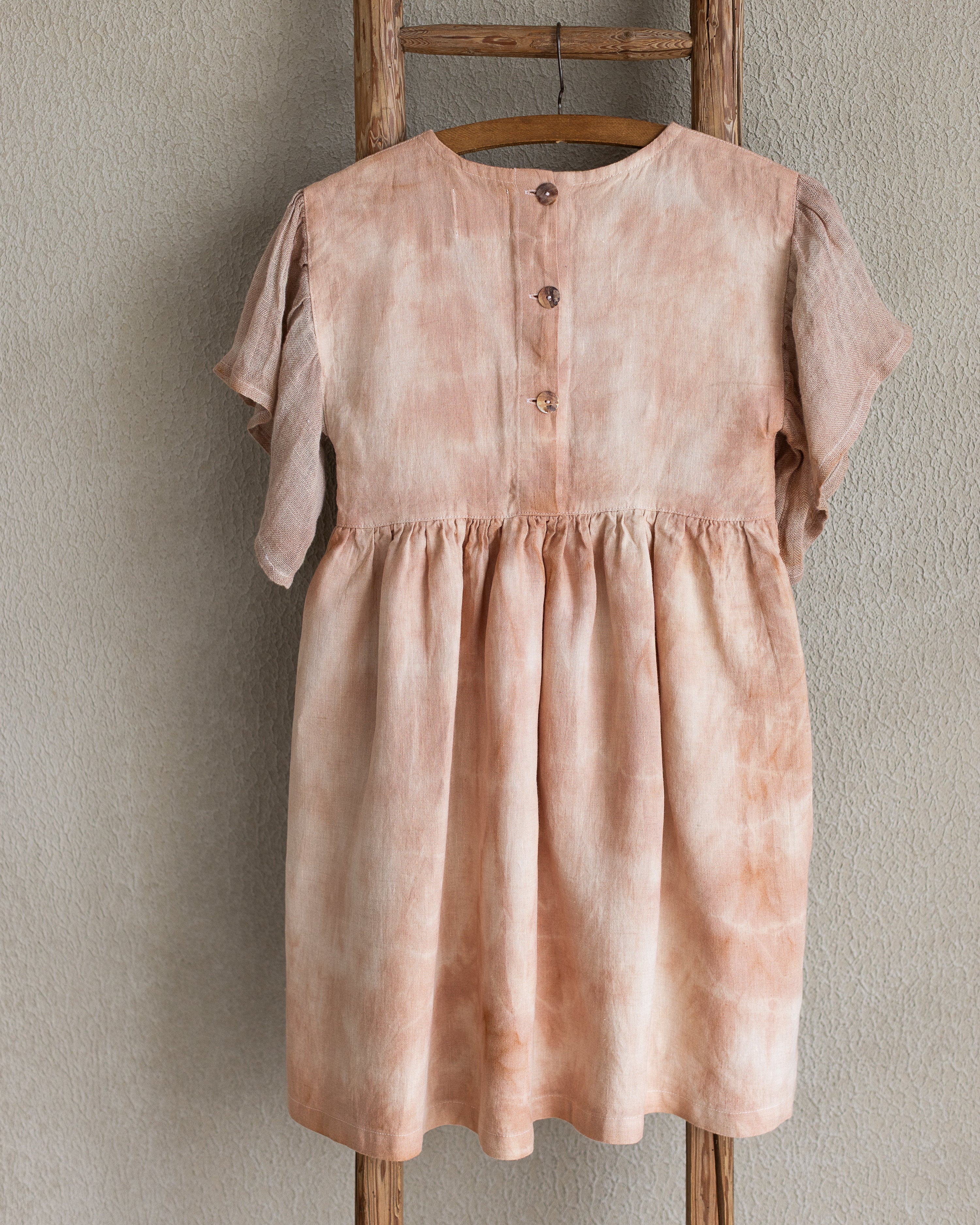 Peach pink linen tie-dye dress on a wooden hanger against a beige wall