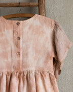 Peach pink linen tie-dye dress with buttons on a wooden hanger against a plain wall