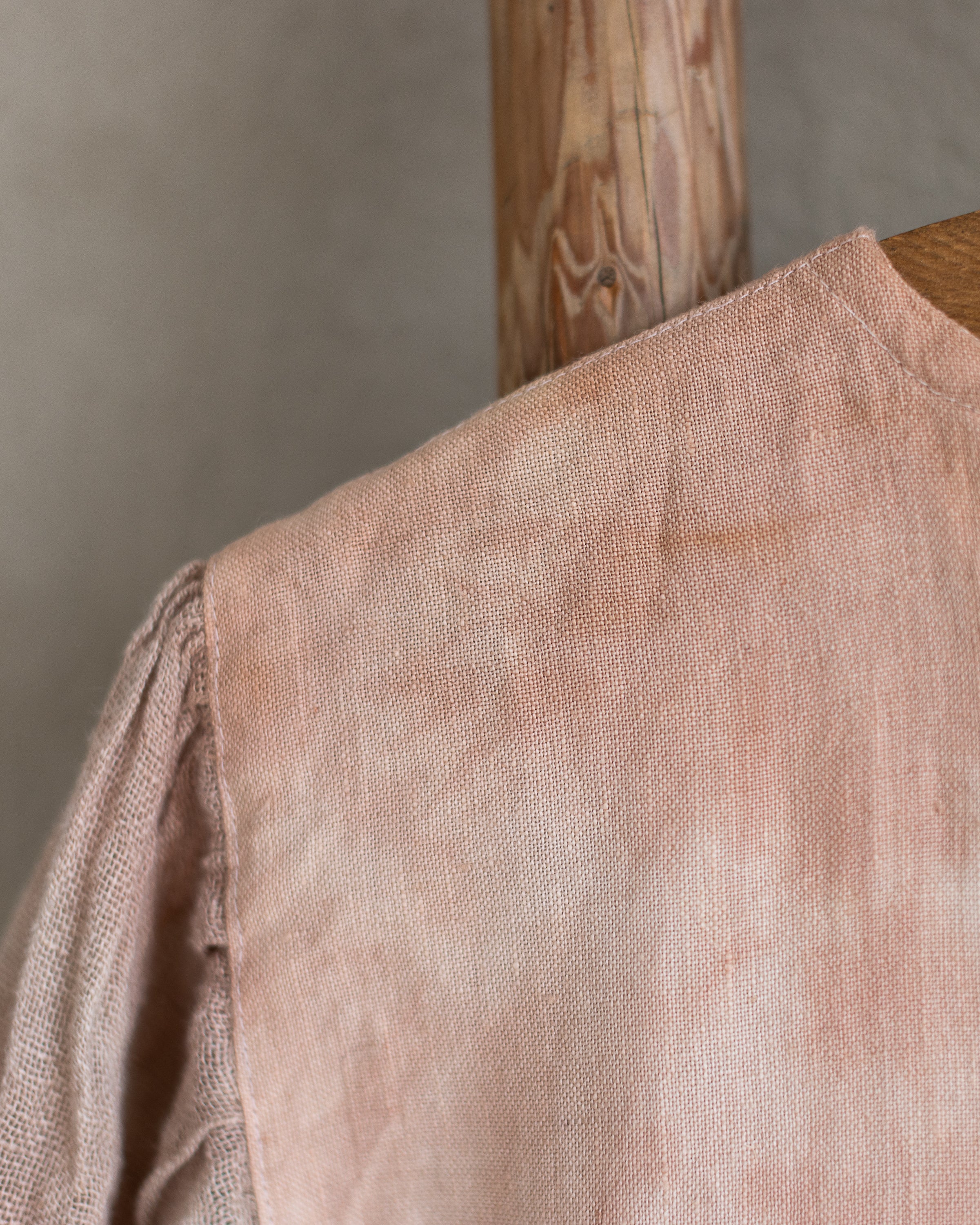 Peach pink linen tie-dye dress on a wooden hanger against a beige wall
