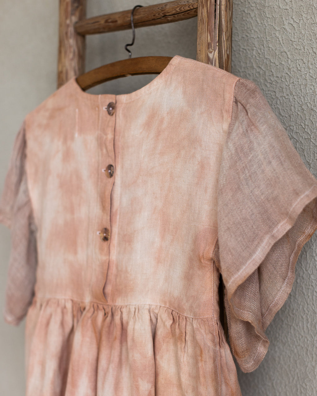 Peach pink linen tie-dye dress on a wooden hanger against a beige wall