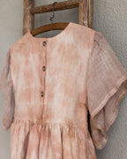 Peach pink linen tie-dye dress on a wooden hanger against a beige wall