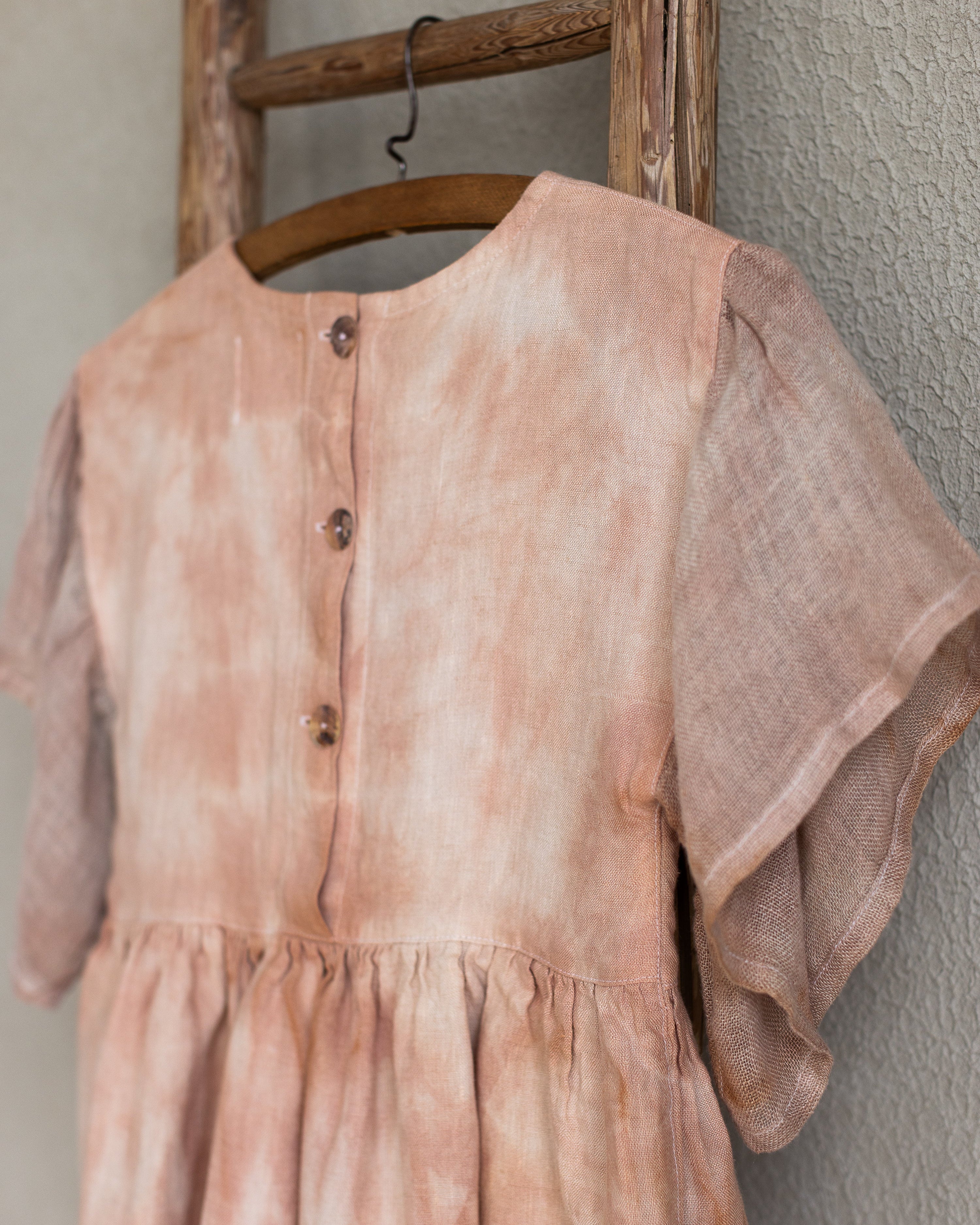 Peach pink linen tie-dye dress on a wooden hanger against a beige wall