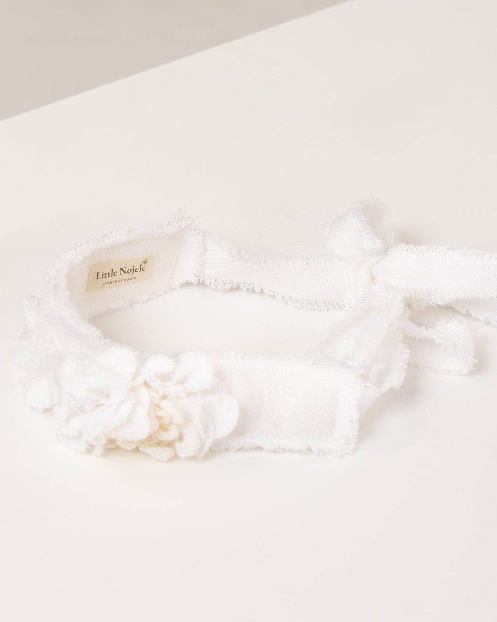 White linen headband with flowers made from fabric scraps on a light beige background