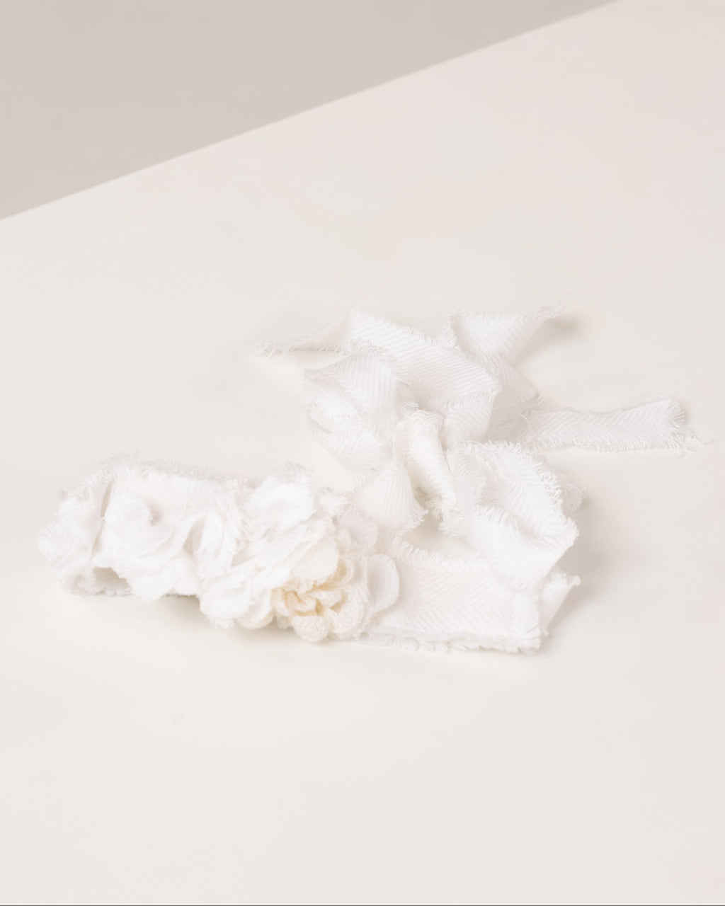 White linen headband with flowers made from fabric scraps on a light beige surface