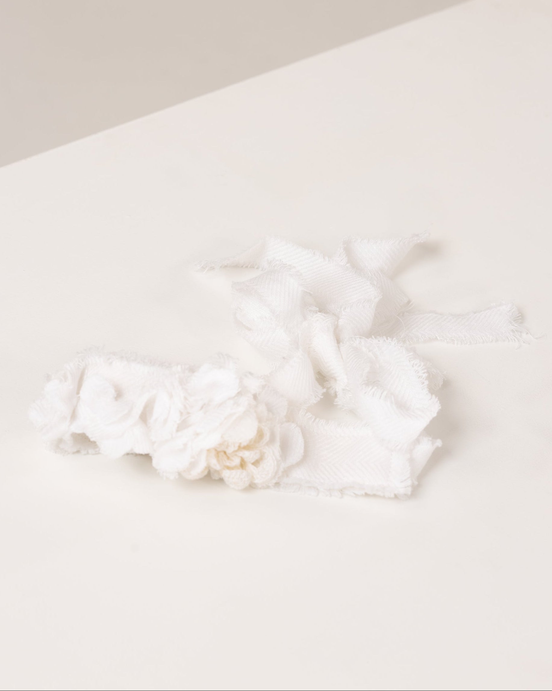 White linen headband with flowers made from fabric scraps on a light beige surface