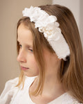 Young girl wearing a white linen headband  with flowers made from scraps against a plain background