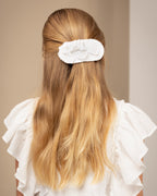 Young girl with long blonde hair wearing a white linen dress against a beige background