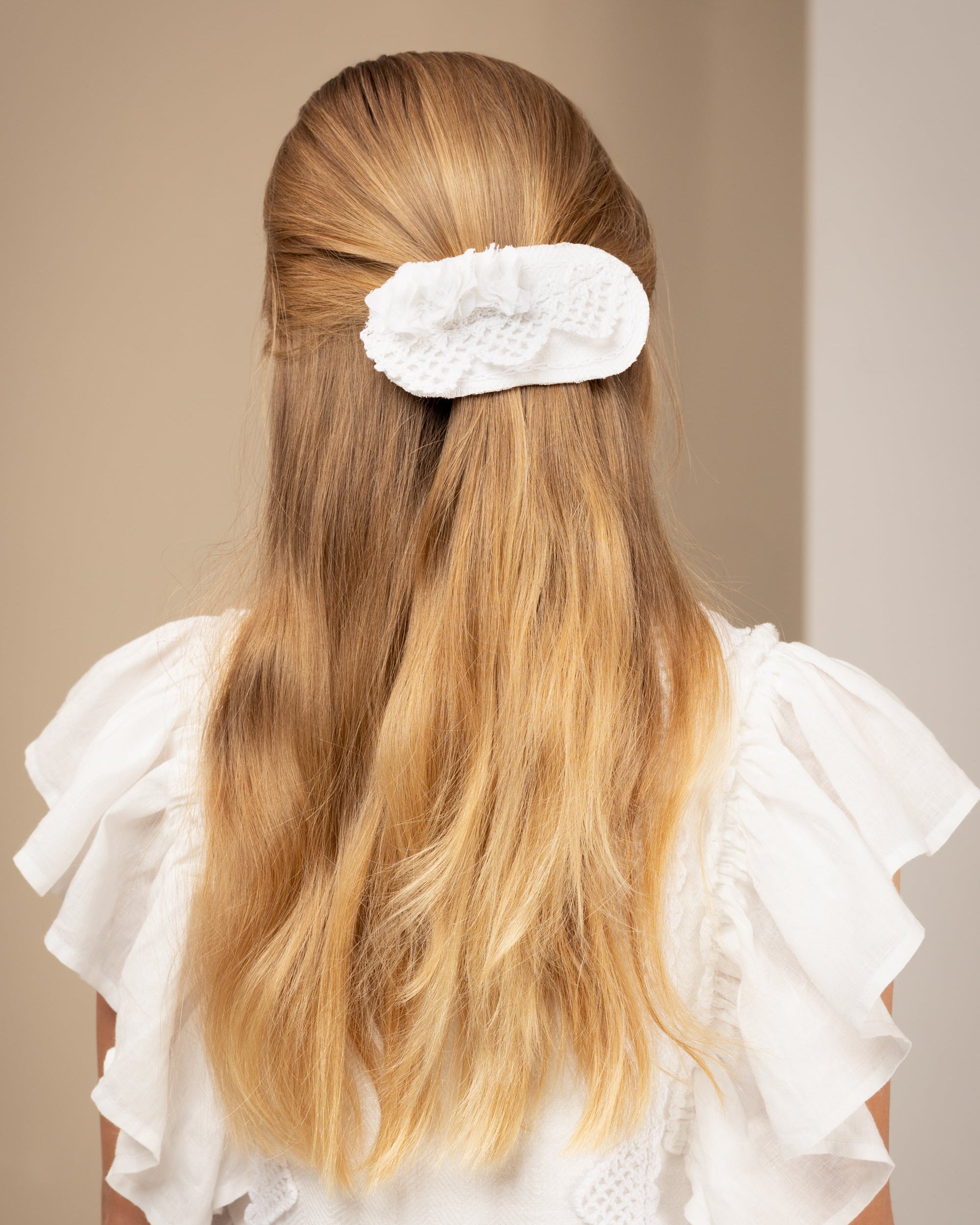 Young girl with long blonde hair wearing a white linen dress against a beige background