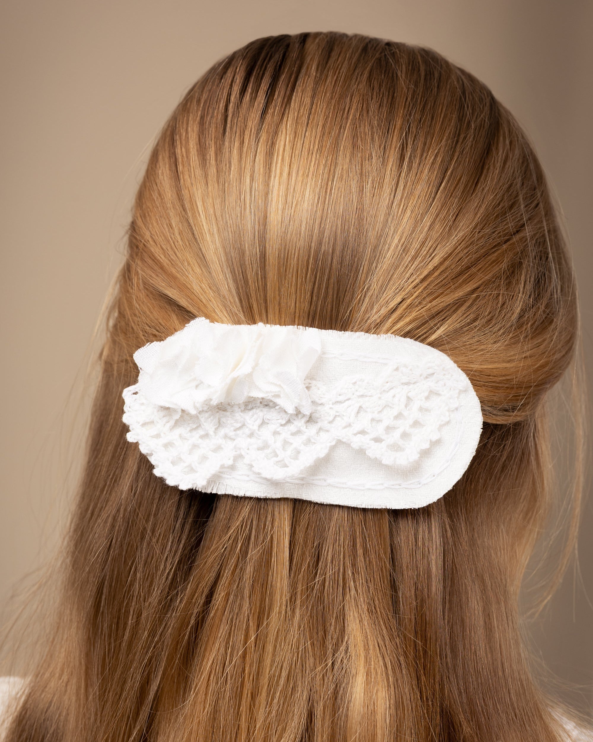 White linen hair clip with crocheted lace and fabric craps flowers on a girls hair against a beige background
