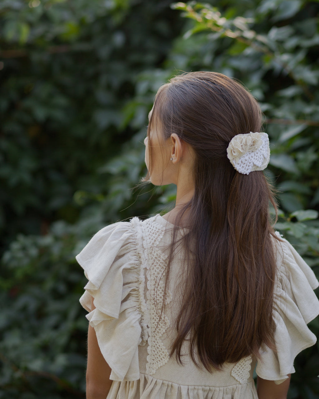 Young girl with a floral hair clip in her hair, standing against a green leafy background