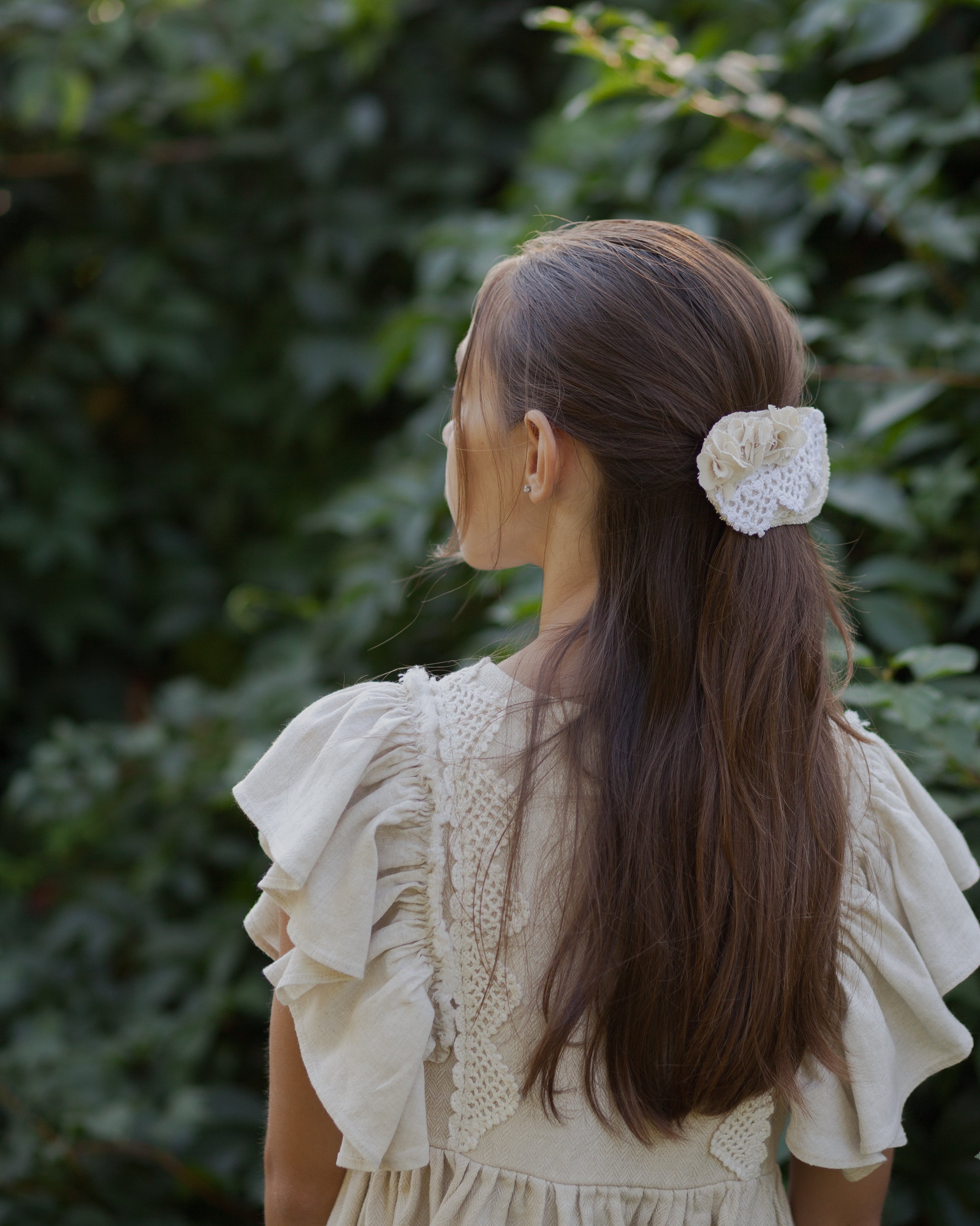 Young girl with a floral hair clip in her hair, standing against a green leafy background