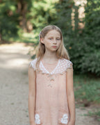 Young girl in a pink linen dress with crocheted ace details standing outdoors on a path.