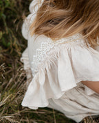 Close-up of a girl wearing a beige linen dress with crochet lace in a natural setting