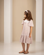 Young girl in a light linen dress standing in an archway with a neutral background
