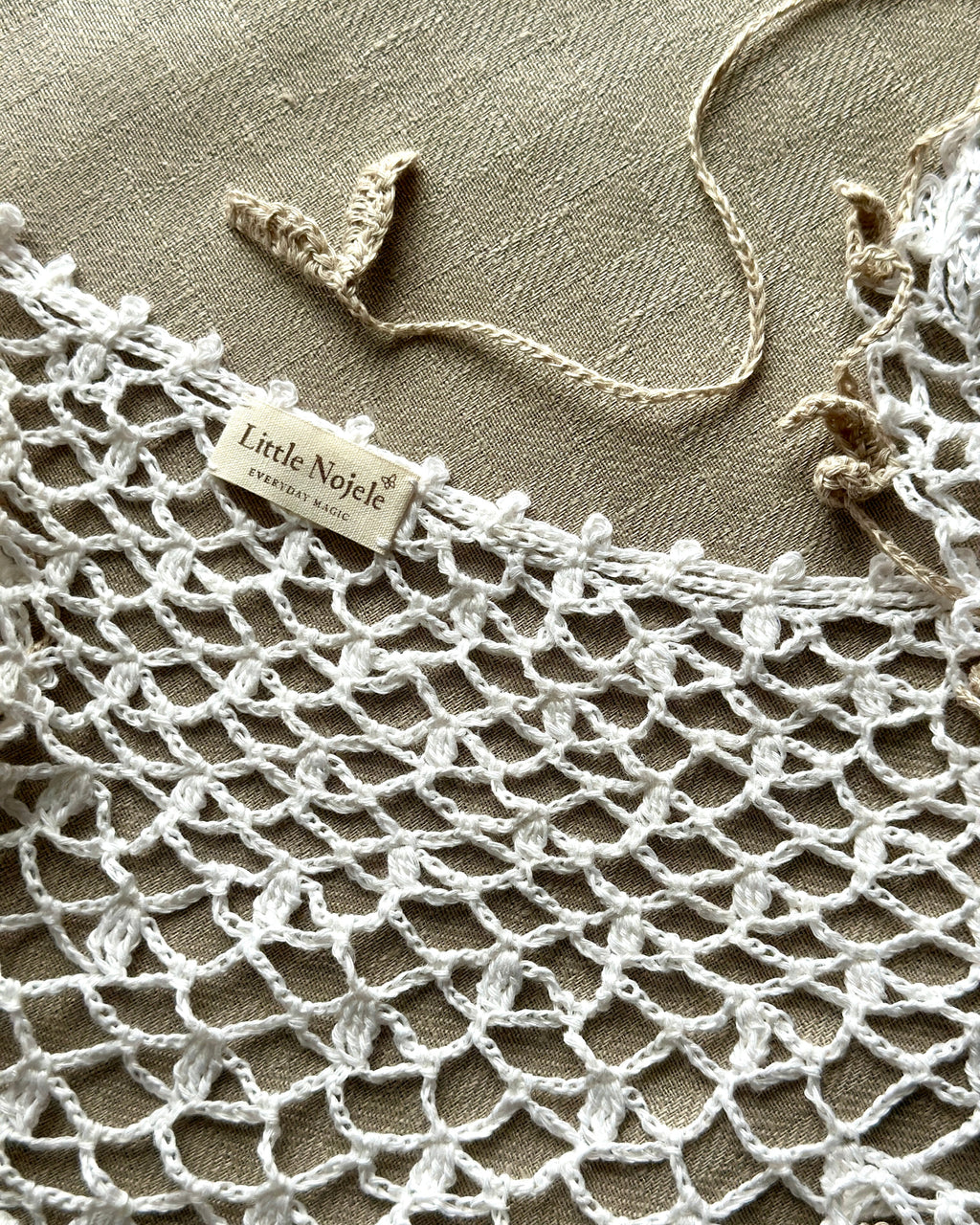 Close-up of a crocheted white linen collar with 'Little Nolete' label on a beige background