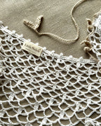 Close-up of a crocheted white linen collar with 'Little Nolete' label on a beige background