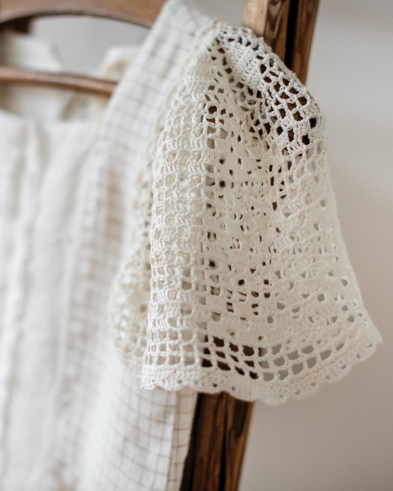 White linen dress with crocheted lace sleeves trim draped over a wooden chair.