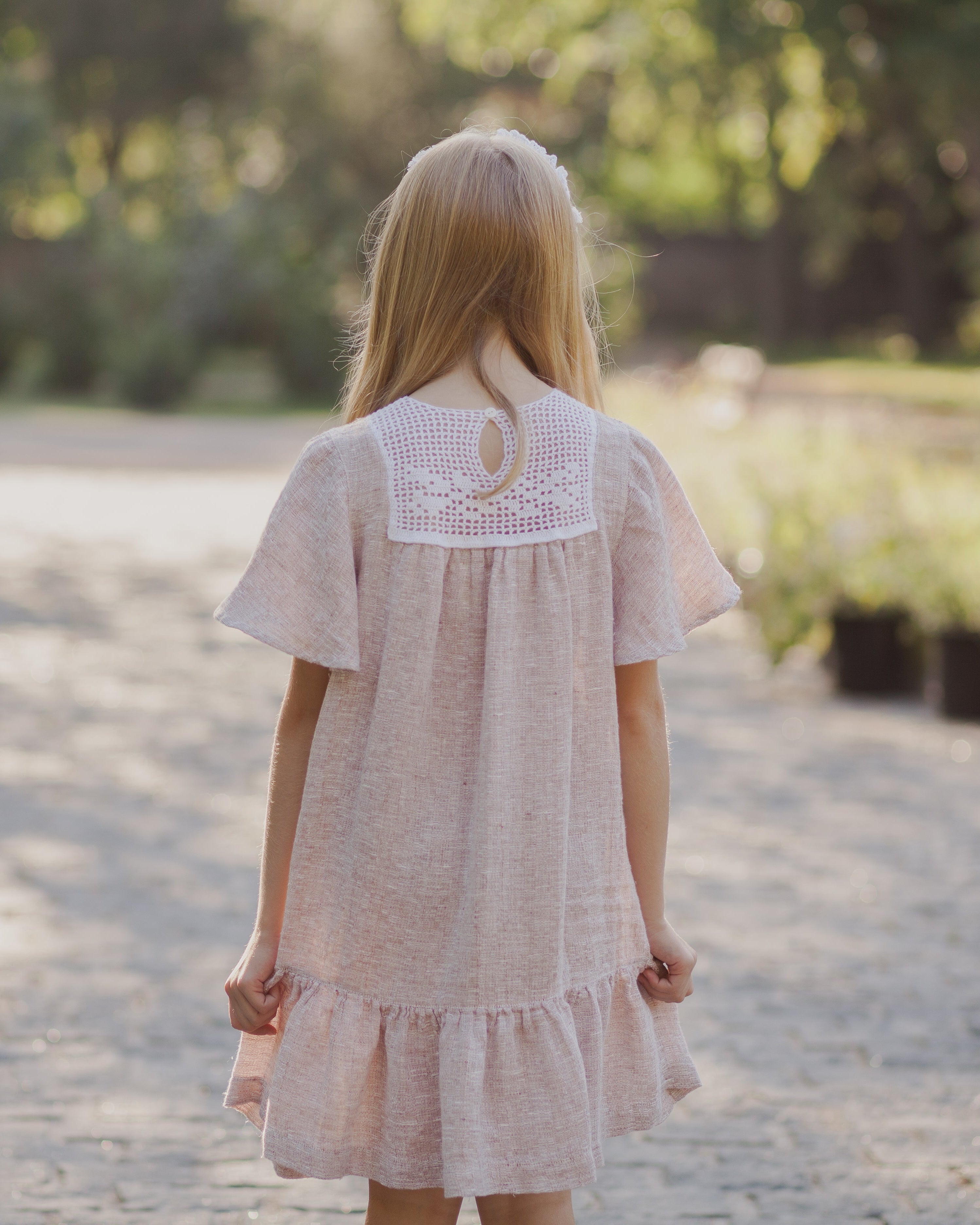 Woman in a light linen dress walking away on a path in a garden