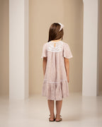 Young girl wearing a light pink linen dress with lace details in an archway.