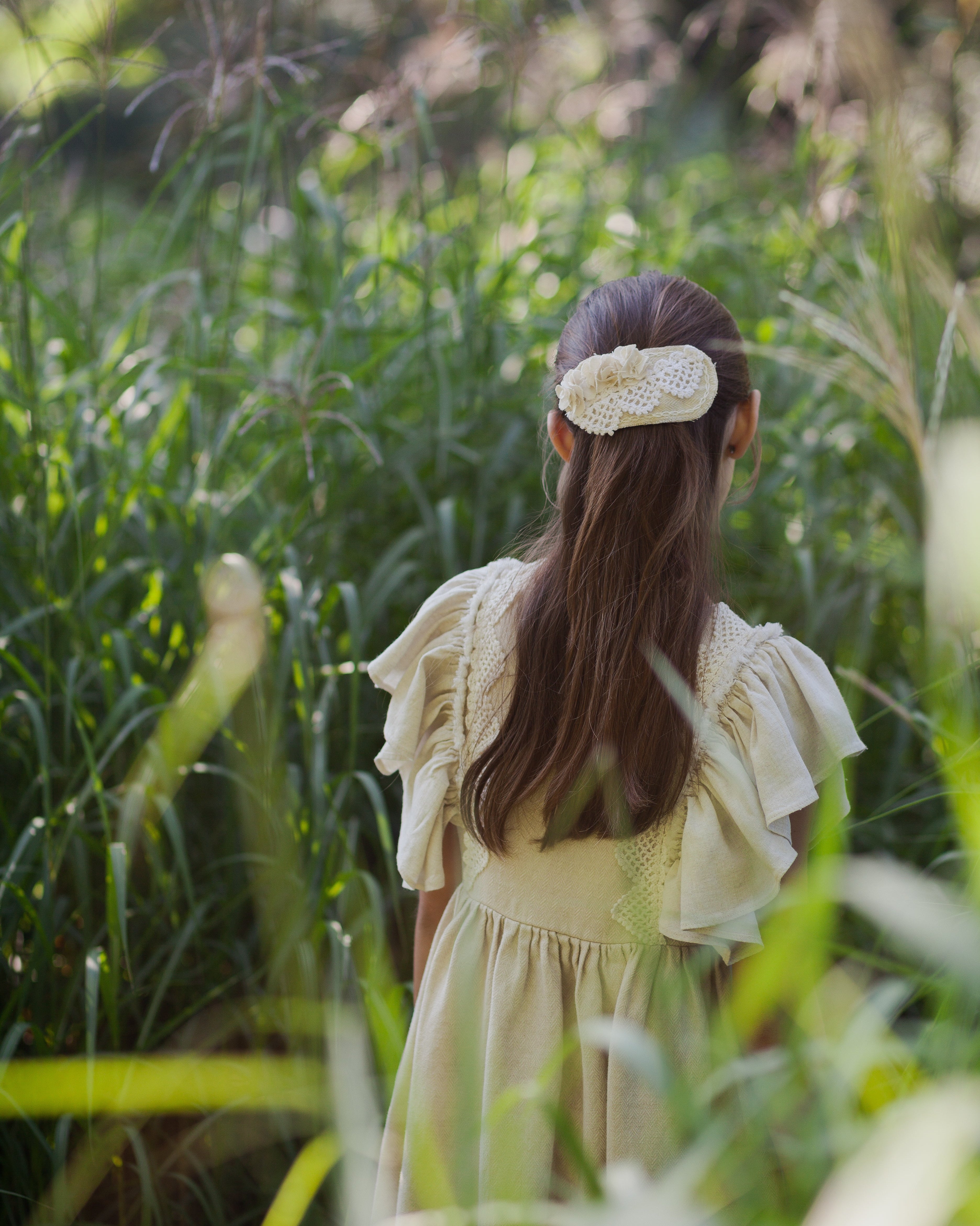 Young girl in a beige linen dress standing in a grassy field with a blurred background
