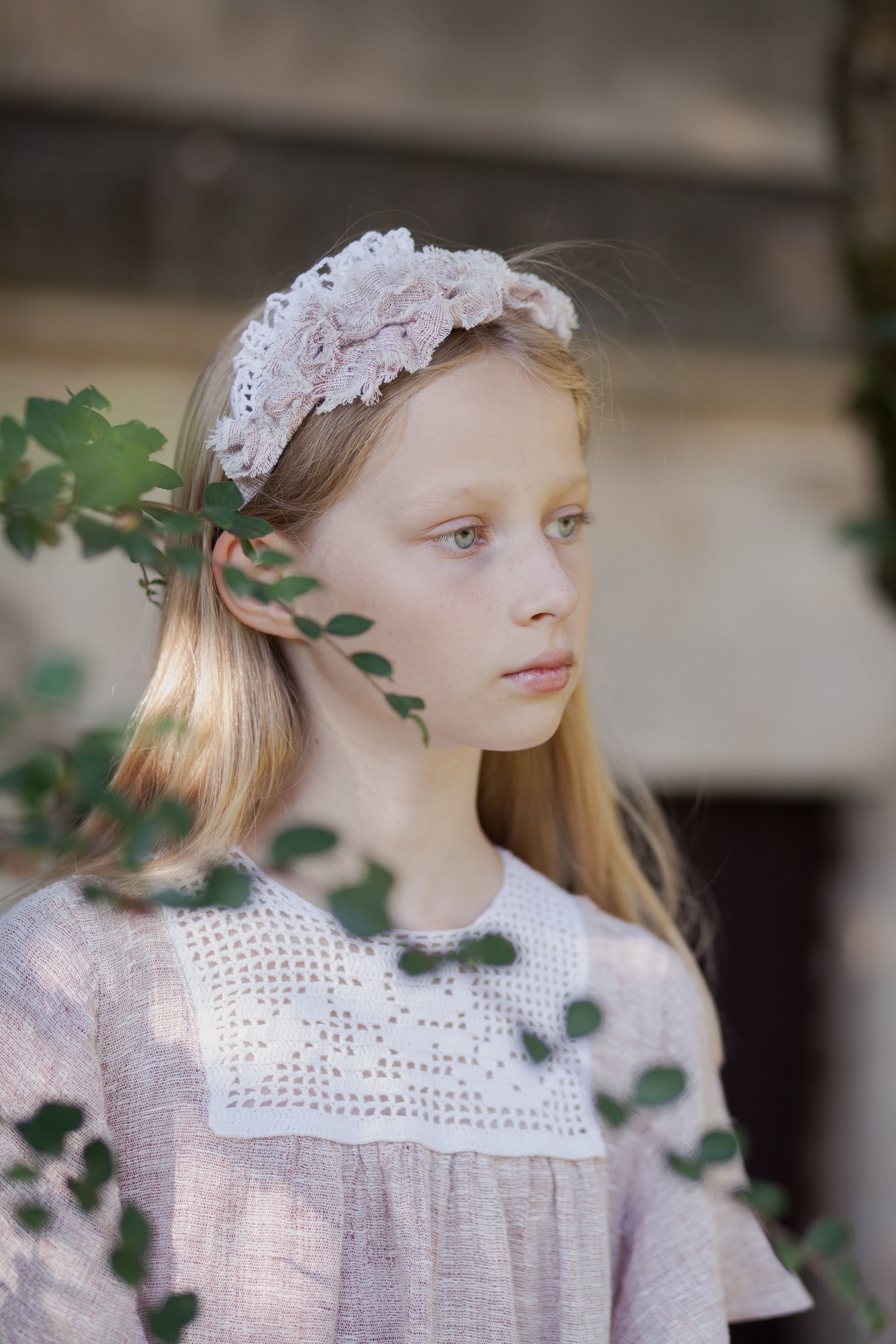 Young girl wearing a lace headband with greenery in the foreground