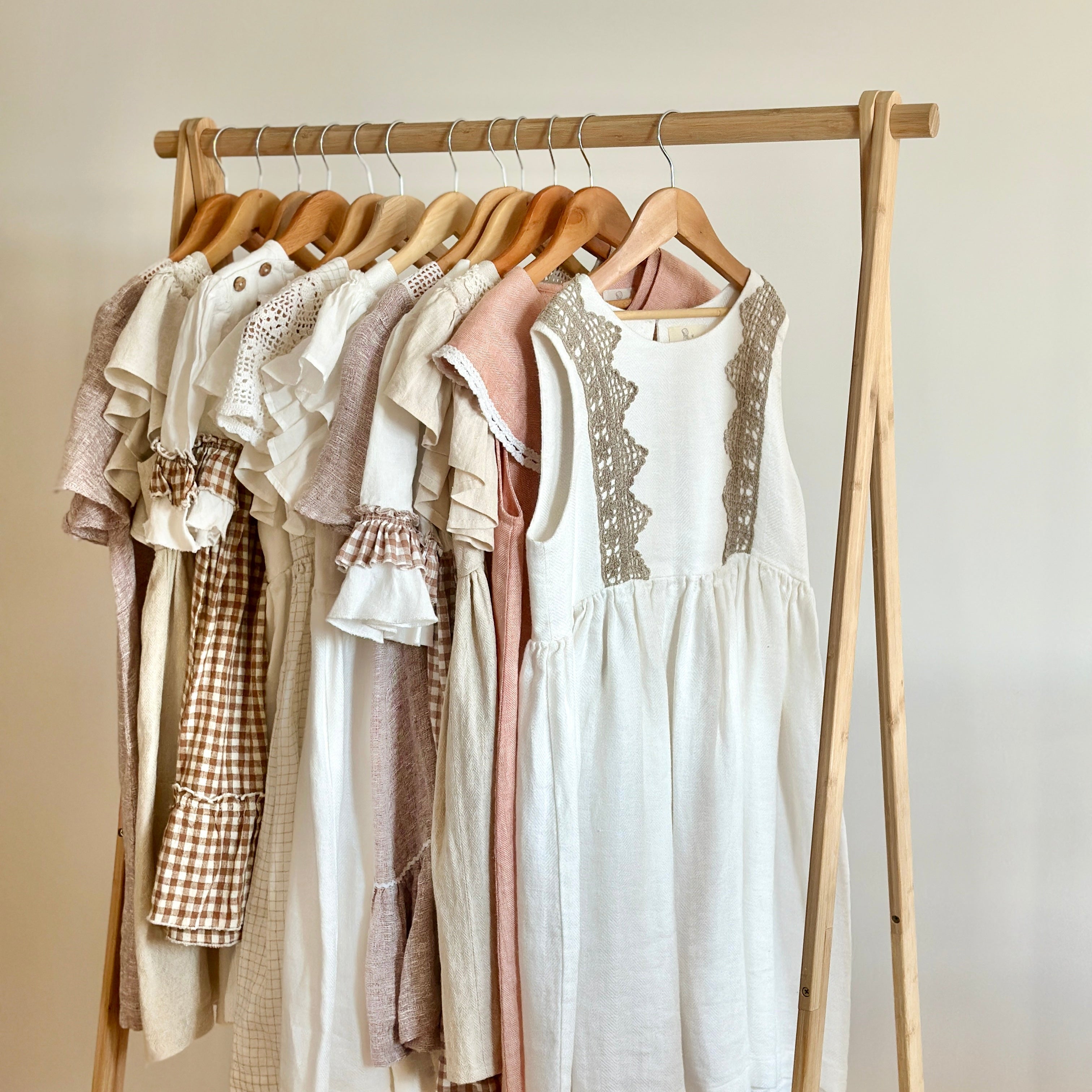 Wooden clothing rack with linen girls dresses against a white wall