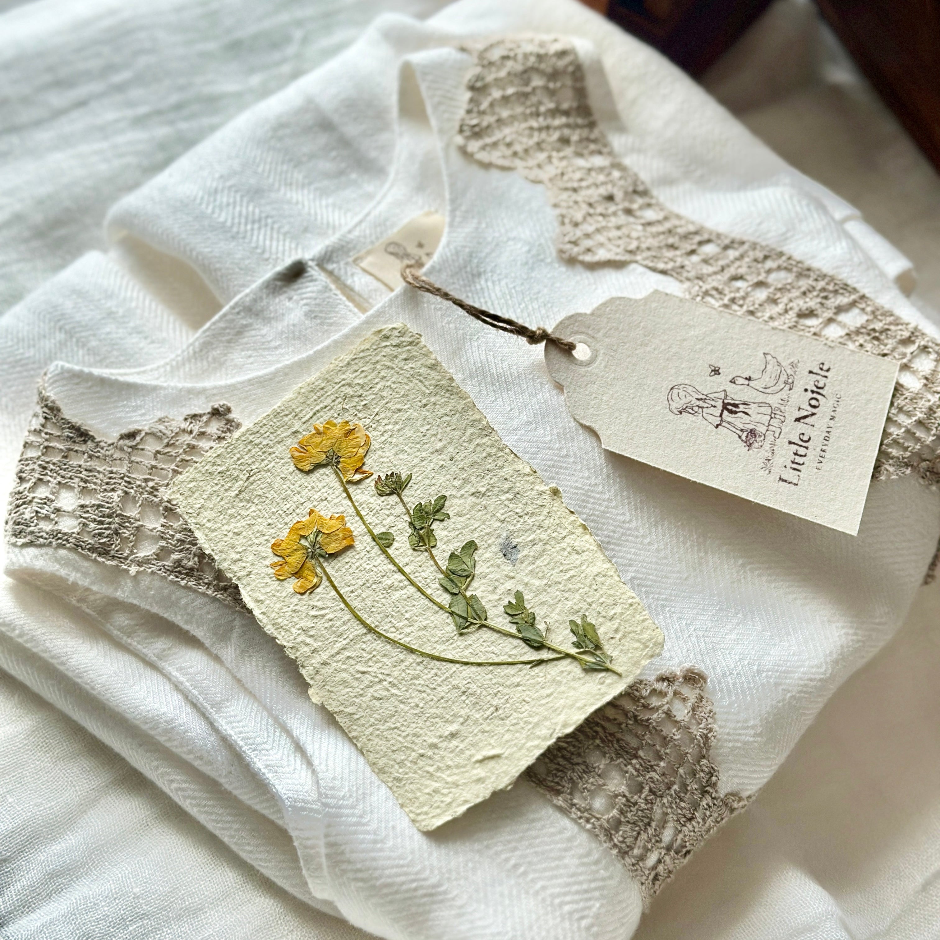 Folded white linen dress with crochet lace details and a card with yellow flowers on a white surface.