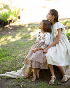 Two young girls in linen dresses sitting on a log in a natural setting
