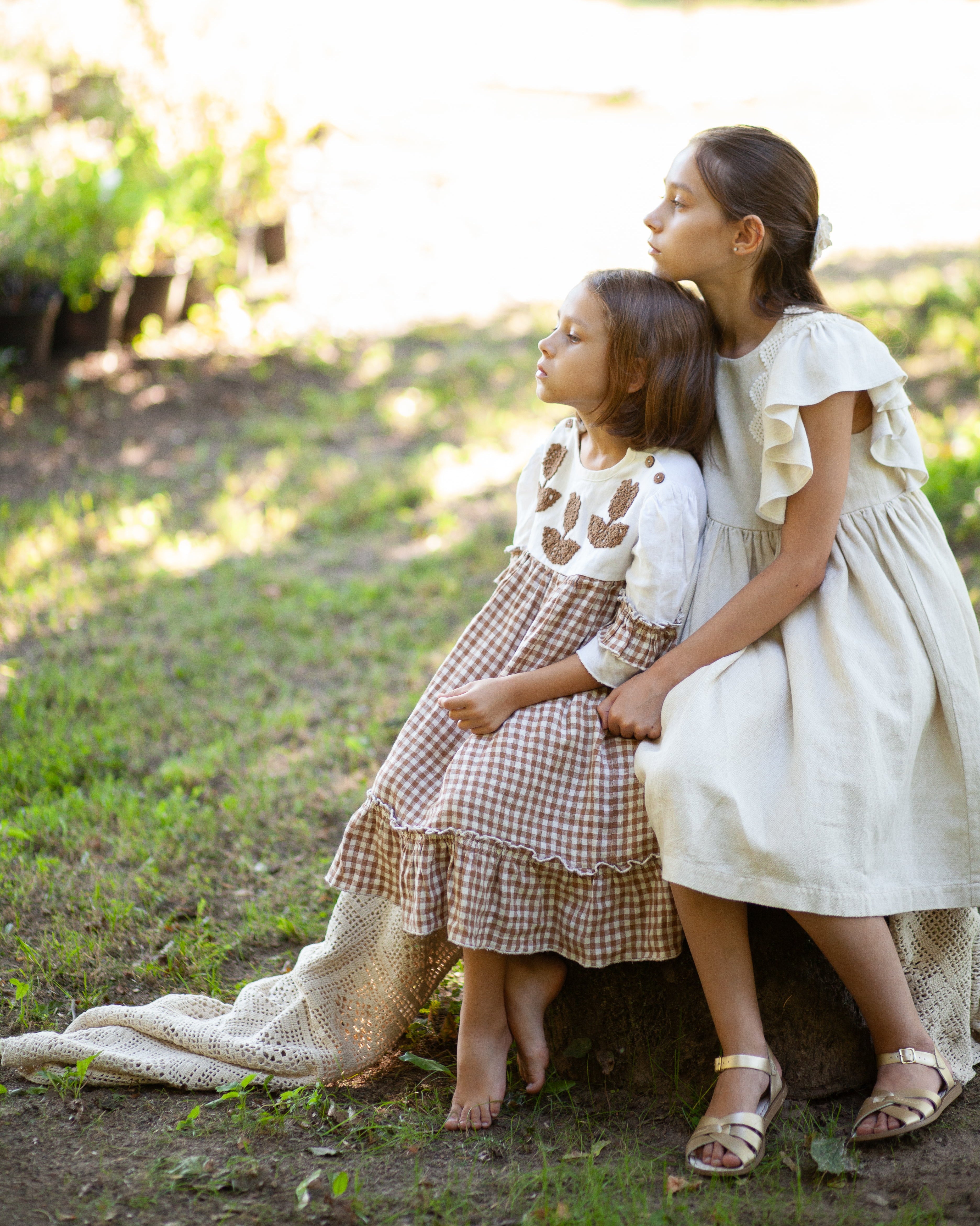 Two young girls in linen dresses sitting on a log in a natural setting