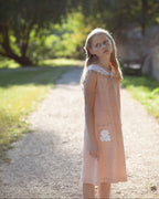 Young girl in a peach linen dress standing on a path with trees in the background