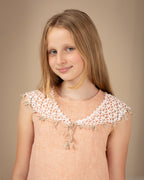 Young girl wearing a peach linen dress with crocheted linen collar against a beige background